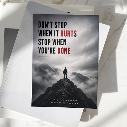 Don't Stop When It Hurts Stop When You're Done motivational poster displayed on a desk, featuring a lone figure standing on a mountain peak, premium inspirational wall art print.