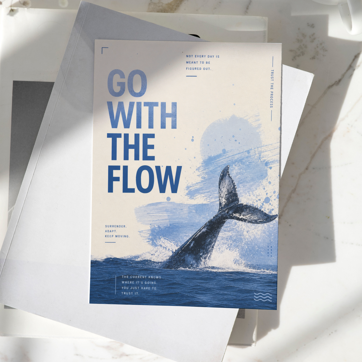 Go With The Flow motivational poster displayed on a desk, featuring a whale tail emerging from the ocean and calming blue artwork, premium inspirational wall art print.