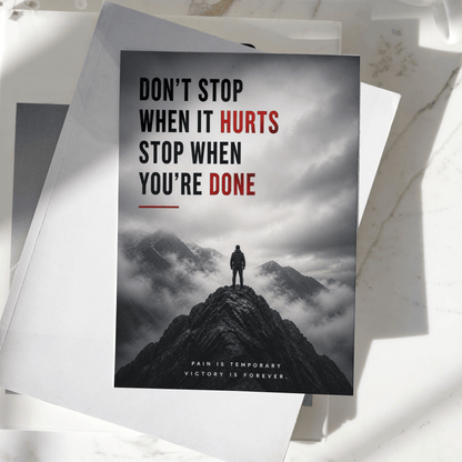 Don't Stop When It Hurts Stop When You're Done motivational poster displayed on a desk, featuring a lone figure standing on a mountain peak, premium inspirational wall art print.